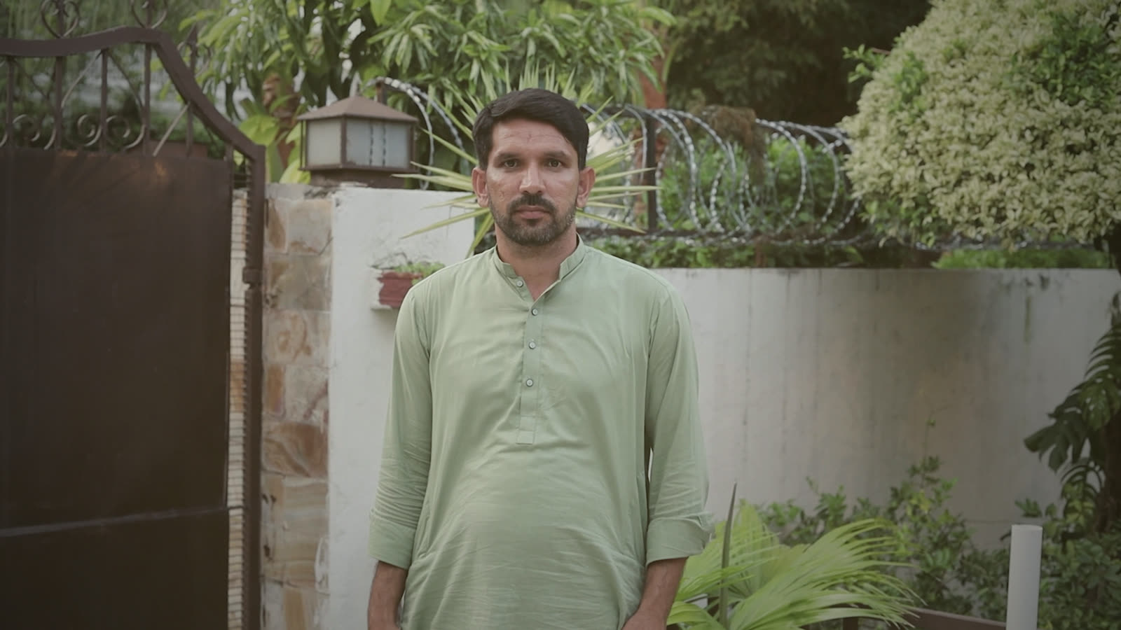 Muhammad Waqas standing at an ivy-covered wall by the gate, looking at the camera